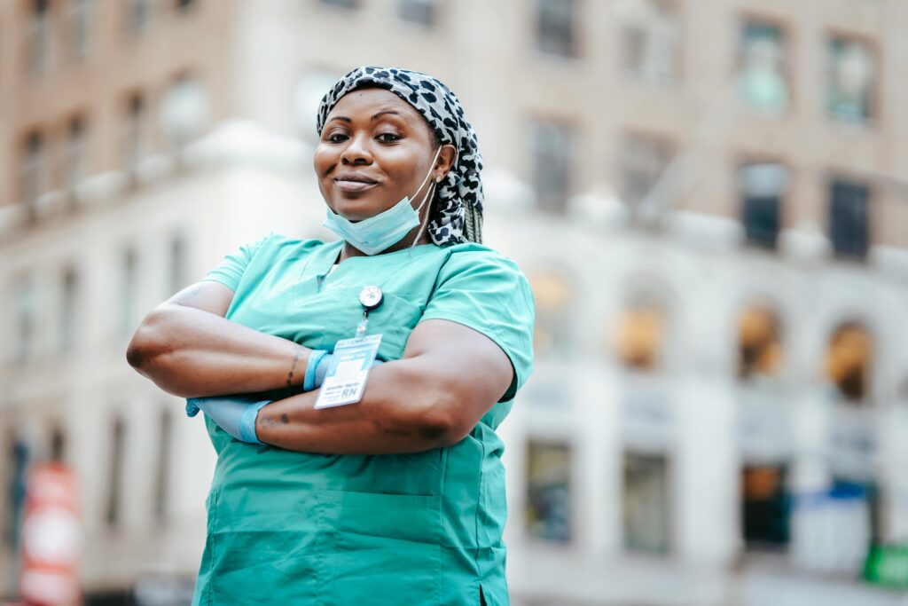 pexels-photo-6098047-6098047 Proud nurse with arms crossed, in uniform, outdoors, urban setting, showing confidence and professionalism.